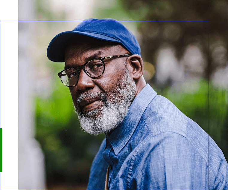 A man with glasses and a cap is standing outside.